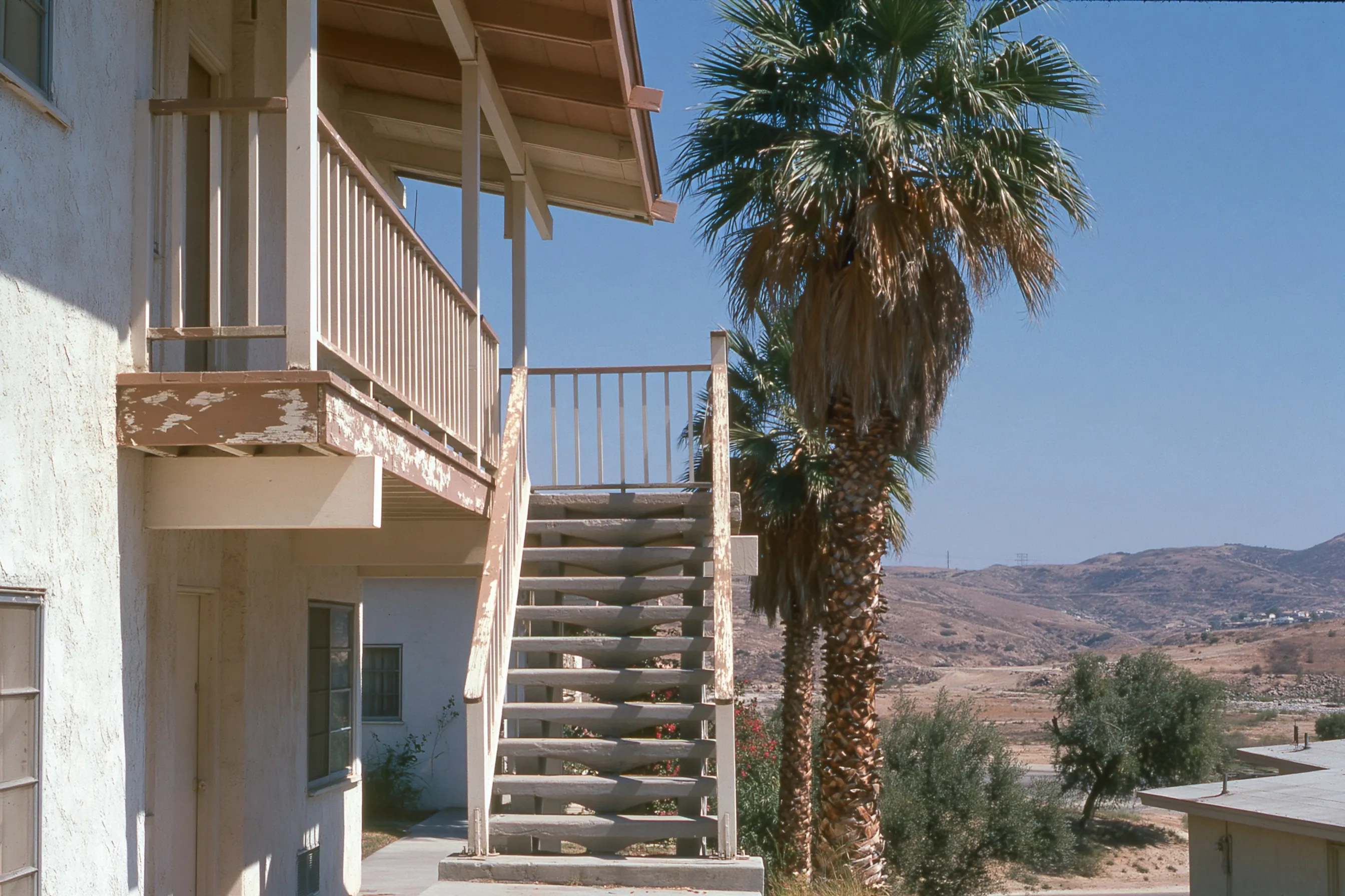 Exterior walkway and concrete stairs of a 1960s two-story stucco apartment building with painted wood railings and trim